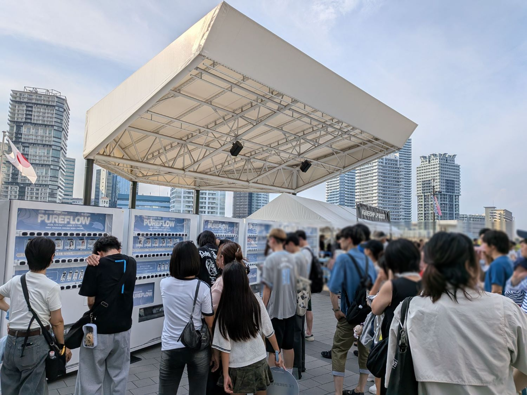イベント会場の広場に設置されたグッズ自動販売機へ、多くの来場者が列をつくる様子