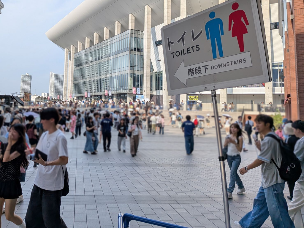 多数の来場者が行き交う広場で、トイレの方向を示す案内標識が設置された様子