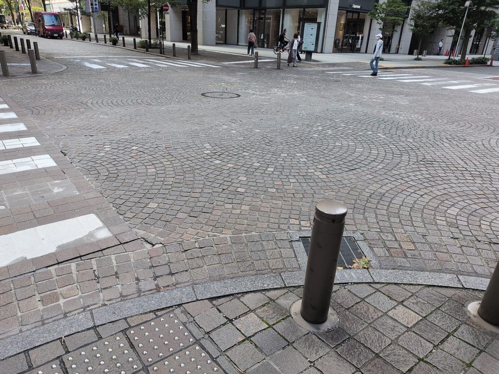 丸の内仲通りの石畳の交差点。扇状の模様を描く石畳が道路一面に敷かれ、奥にビルと歩行者が見える。