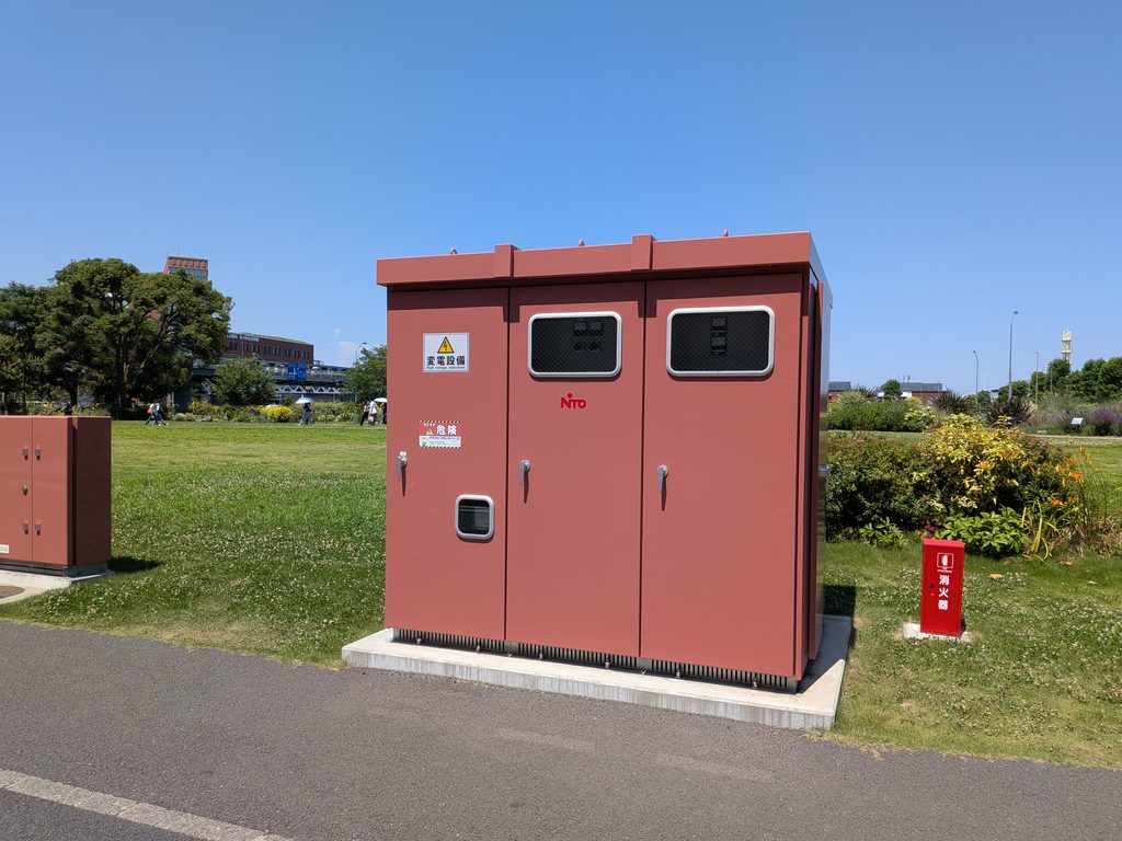 芝生の上に単独で立つ赤茶色の変電設備。「変電設備」「危険」の表示があり、すぐ脇に消火器が置かれている