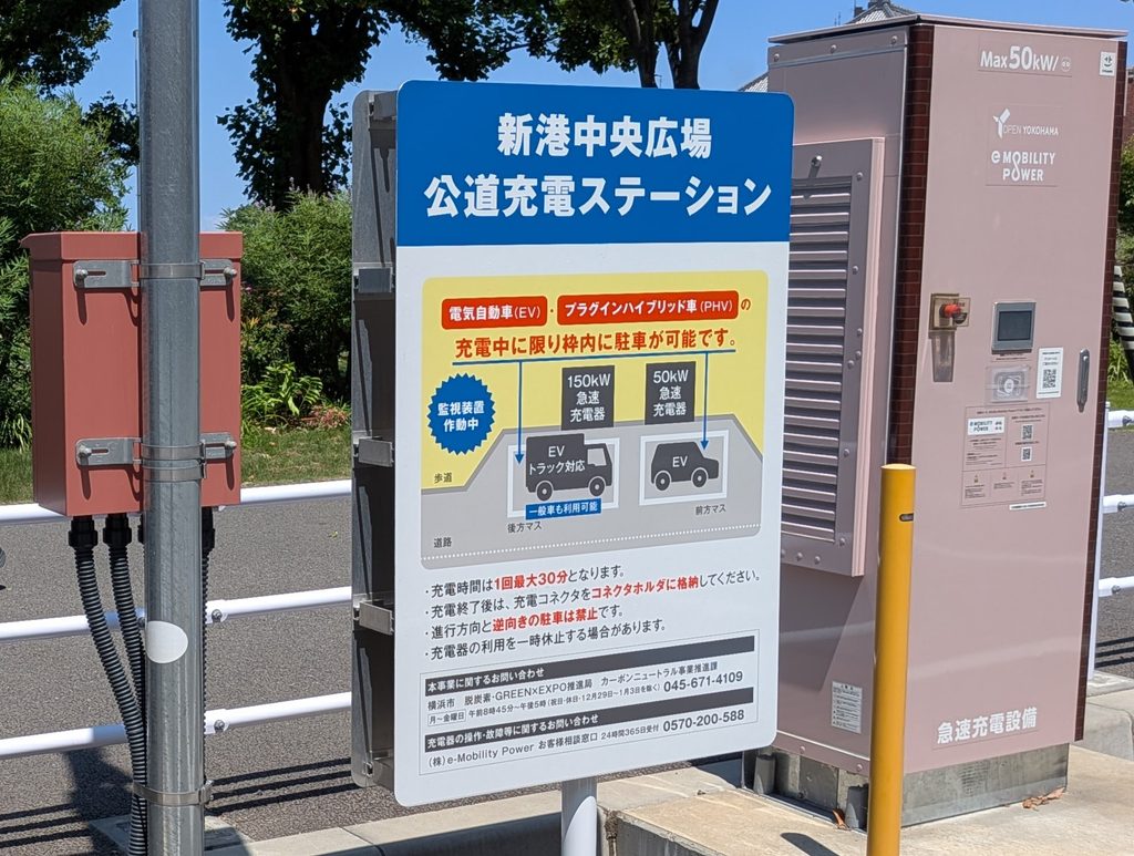 「新港中央広場 公道充電ステーション」の看板。150kWと50kWの充電器の案内図と、充電時間は1回最大30分などの注意書きが並んでいる