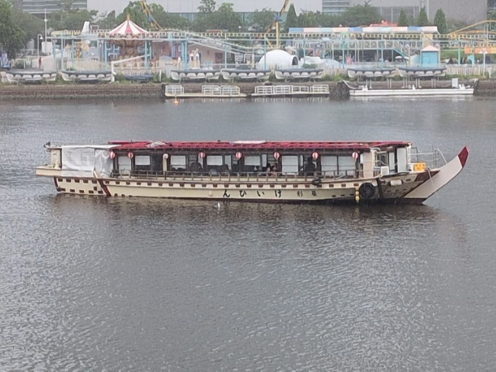 赤い提灯を連ねた屋形船と、背景に見える遊園地の遊具